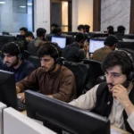 Illustrative image of young call center agents working on computers with headsets in a Pakistani office.